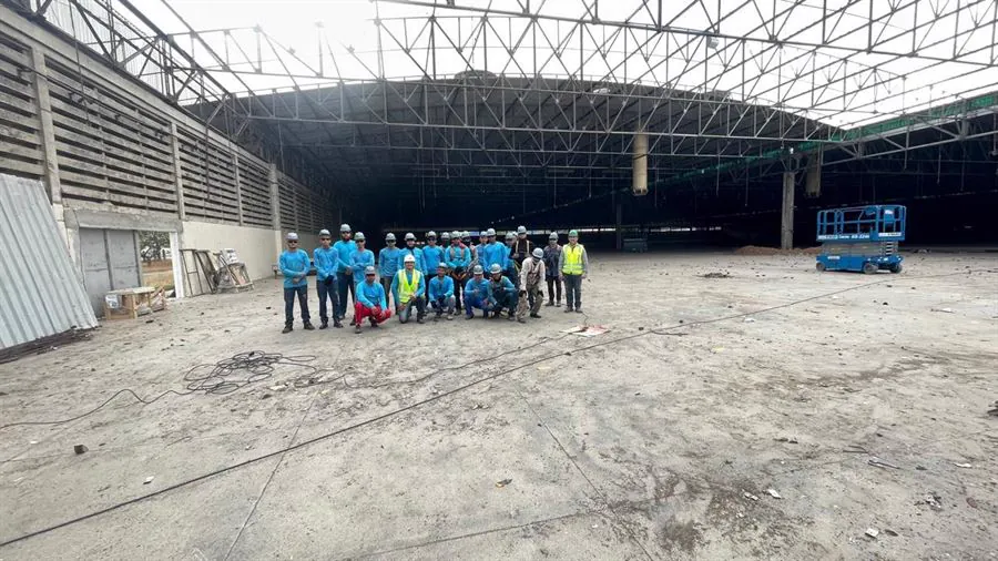 Equipe da A P Silva Construções reunida dentro de um galpão metálico, de uniforme e capacete de segurança