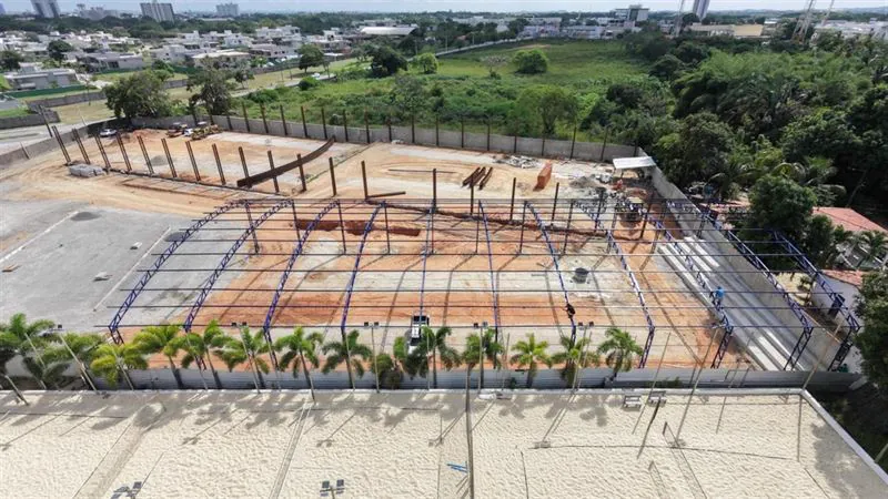 Vista aérea de cobertura metálica montada sobre quadras esportivas, com pórticos de aço pintados de azul