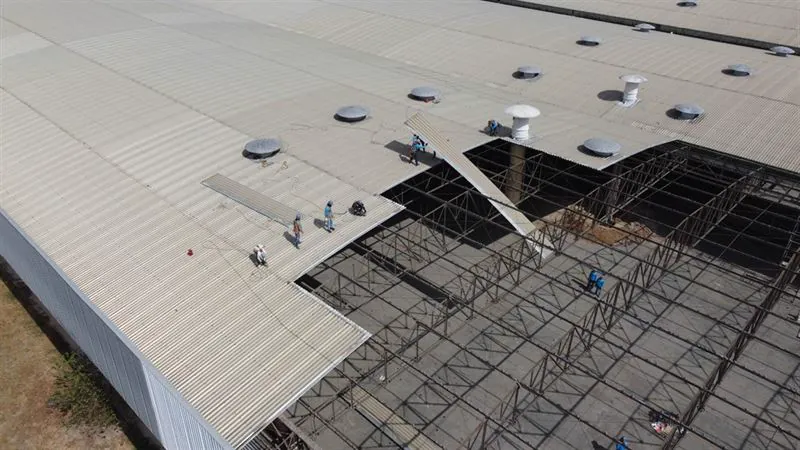 Vista aérea de telhado metálico industrial durante a troca de telhas, com a estrutura treliçada exposta