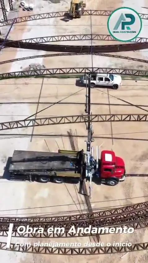 Caminhão munck içando uma treliça em arco durante a montagem da estrutura metálica